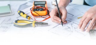 Electrical engineer drawing circuit diagrams with multimeter and pliers on blueprints